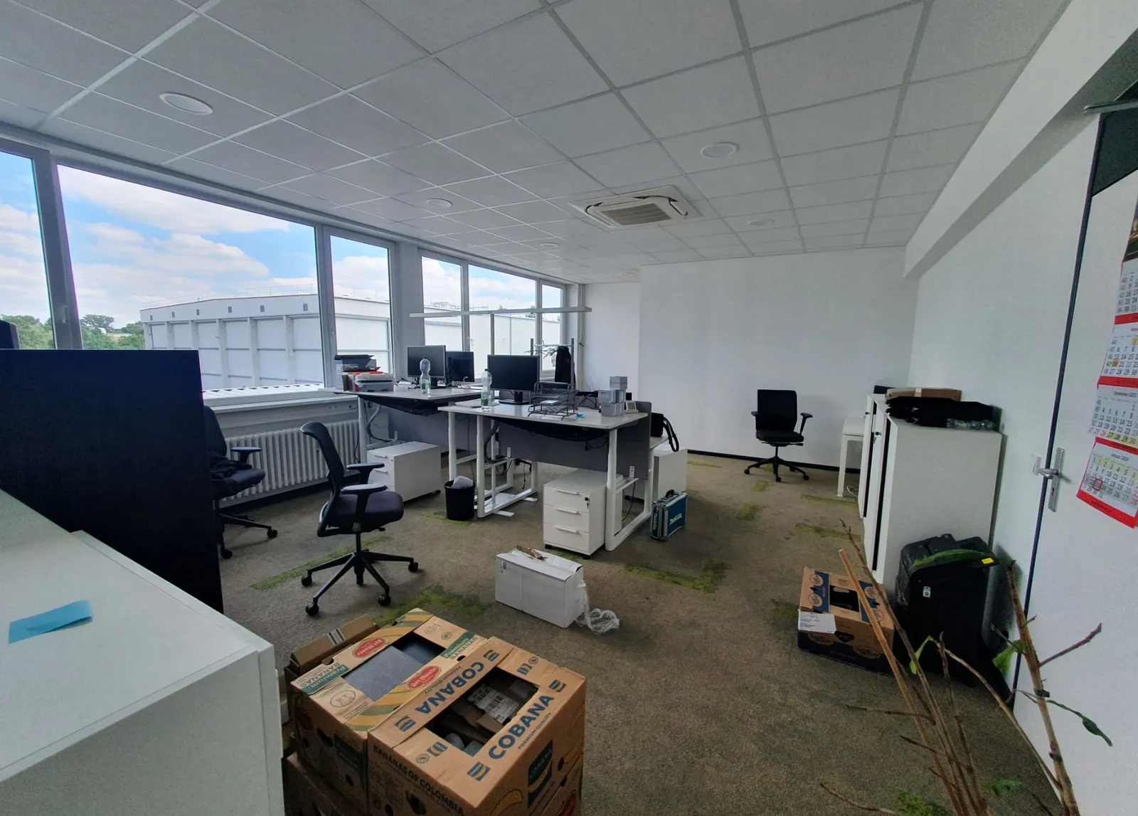 Open-plan Berlin office being cleared, with desks, office chairs, monitors and packed moving boxes