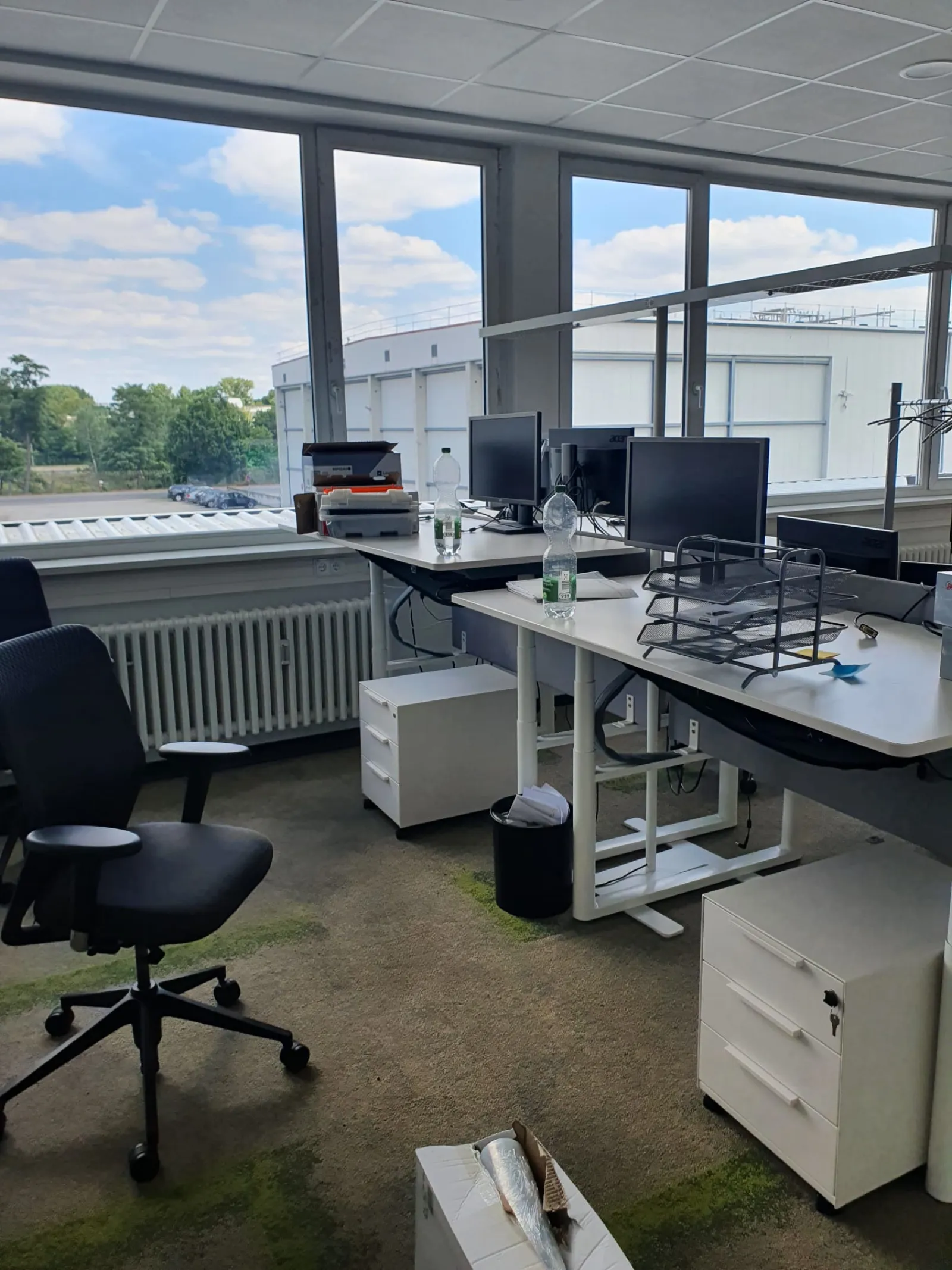 Several office workstations with monitors, mobile pedestals and chairs in front of floor-to-ceiling windows