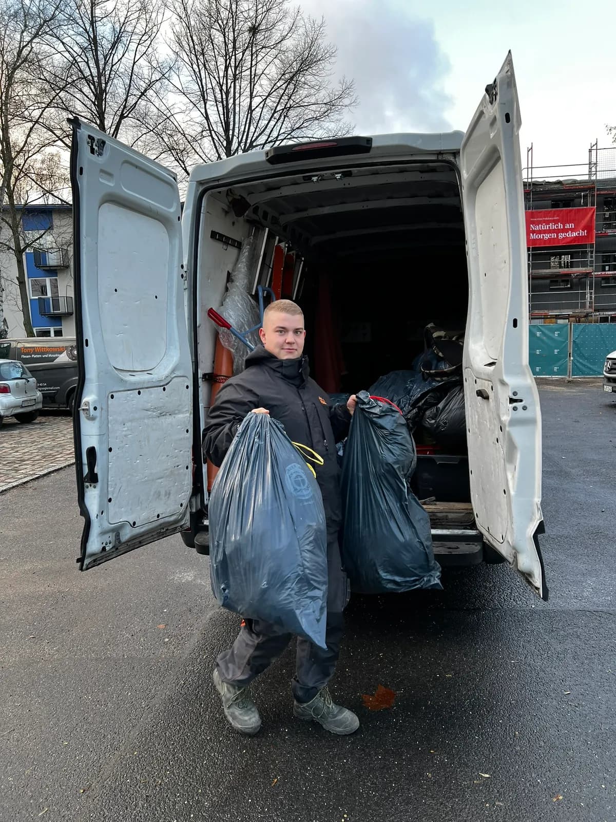 Alles4You-Mitarbeiter trägt zwei Säcke mit gut erhaltenen Sachen aus dem Transporter zur Spende in Berlin
