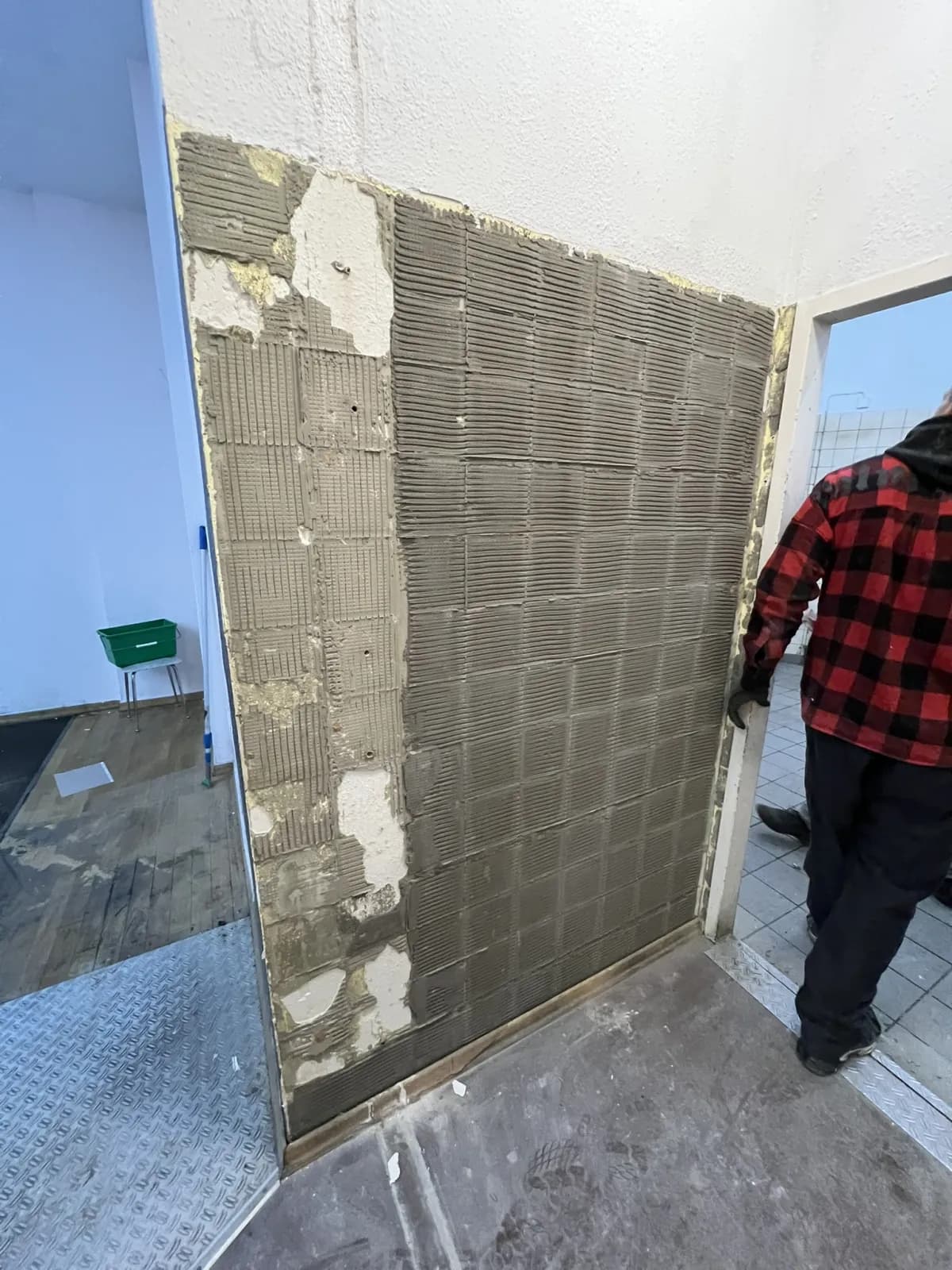 Mitarbeiter im karierten Hemd verlegt Wandfliesen in einem leeren Raum