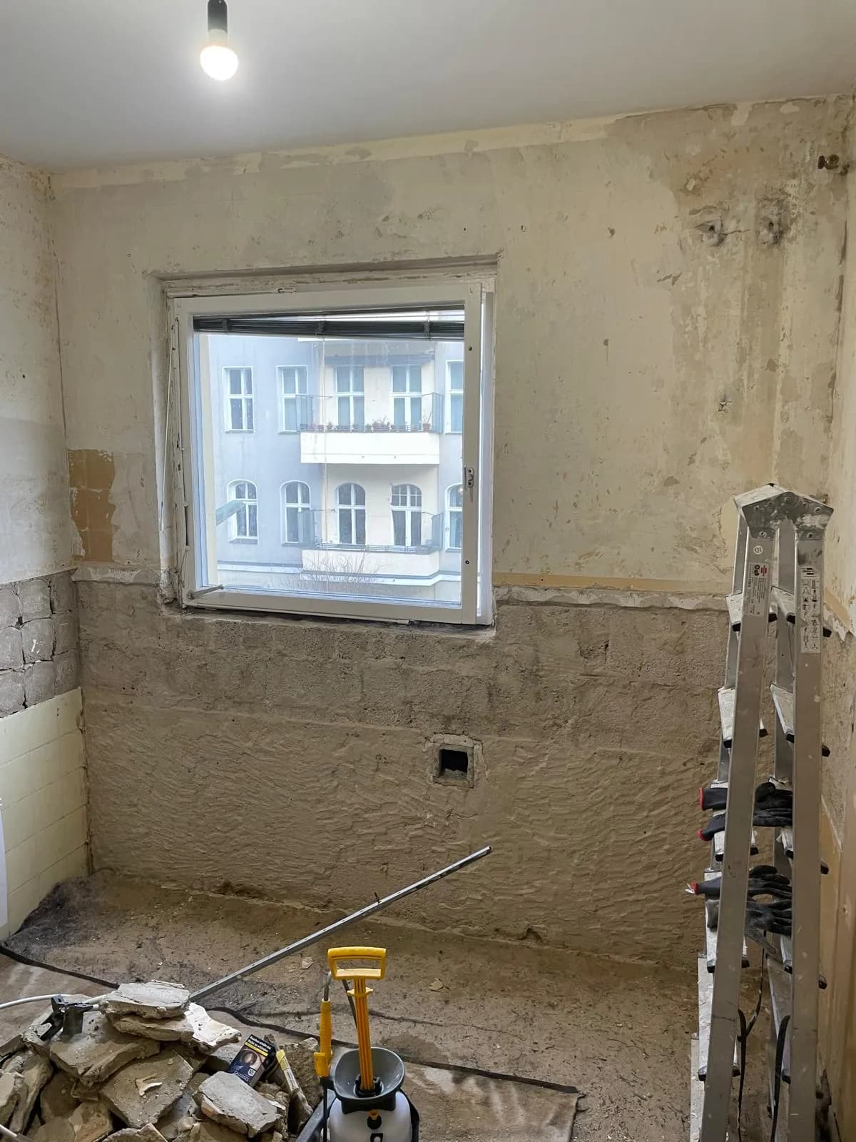 Leerer Raum mit abgerissenen Wänden, freiliegendem Unterputz und Fenster, Leiter und Werkzeug im Raum