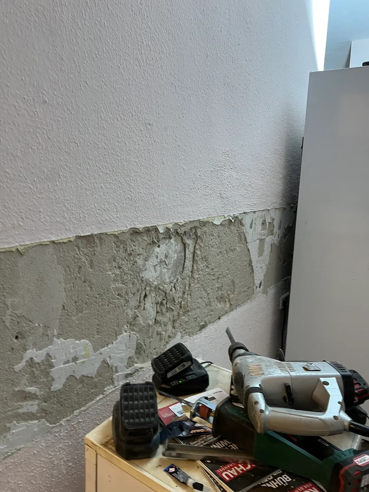 Werkzeug am Einsatzort bei der Renovierung in Berlin: Bohrhammer und Akku auf der Ablage vor frisch verputzter Wand