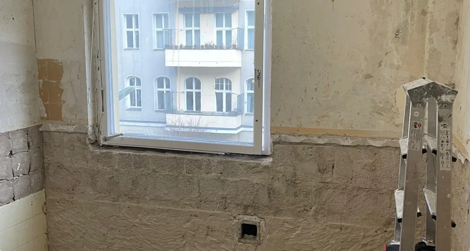 Renovation of a Berlin Altbau apartment with stripped walls, a ladder and tools, window looking onto the neighboring buildings