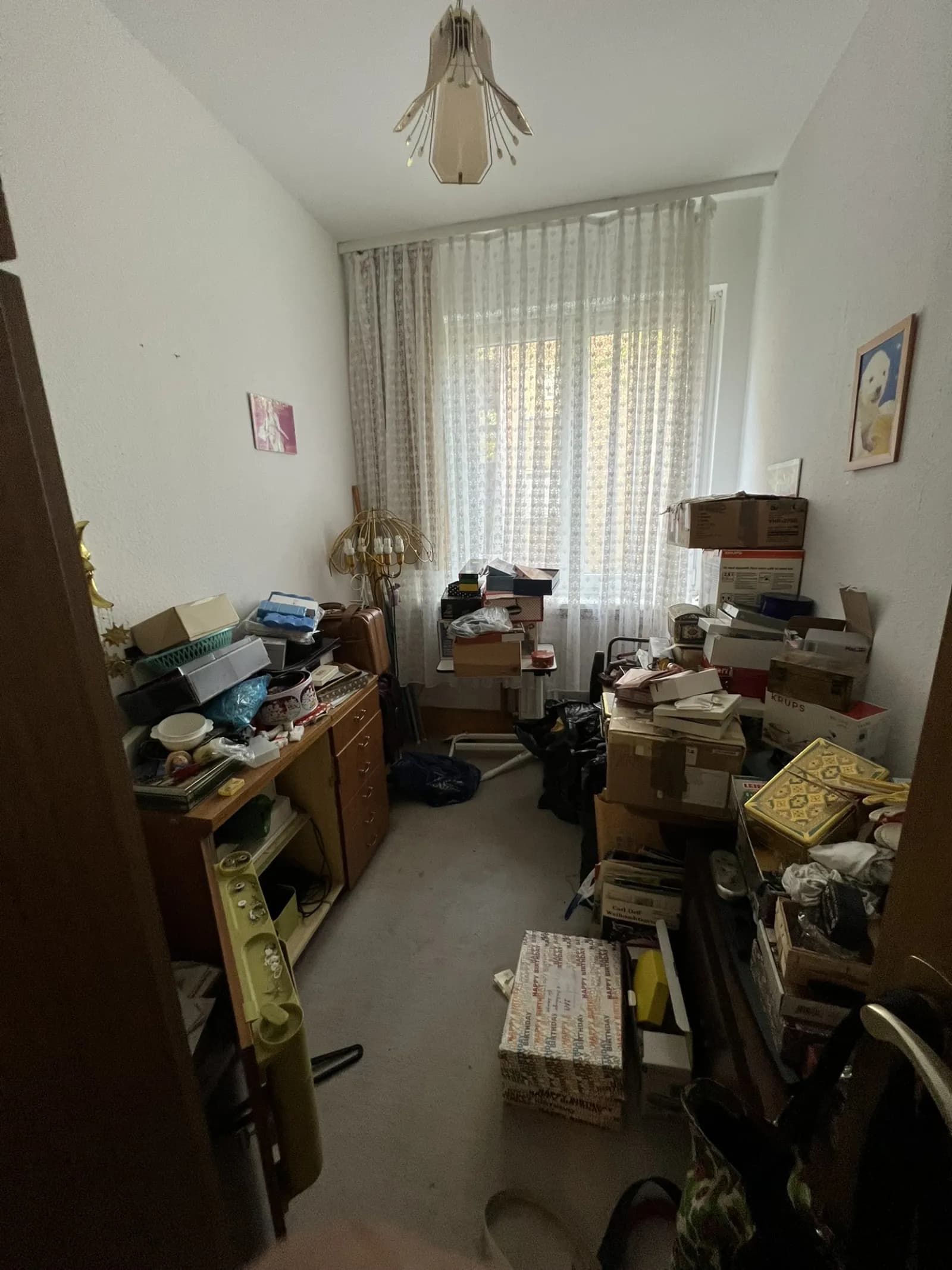 Kleines Zimmer vollgepackt mit Kartons, Regalen und Kleinmöbeln