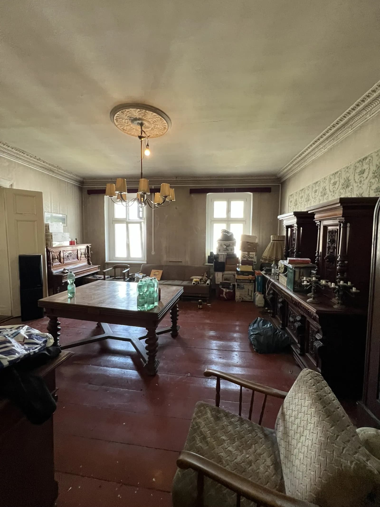 Gründerzeit-Wohnzimmer mit massivem Esstisch, Vertiko und Standuhr vor dem Abtransport
