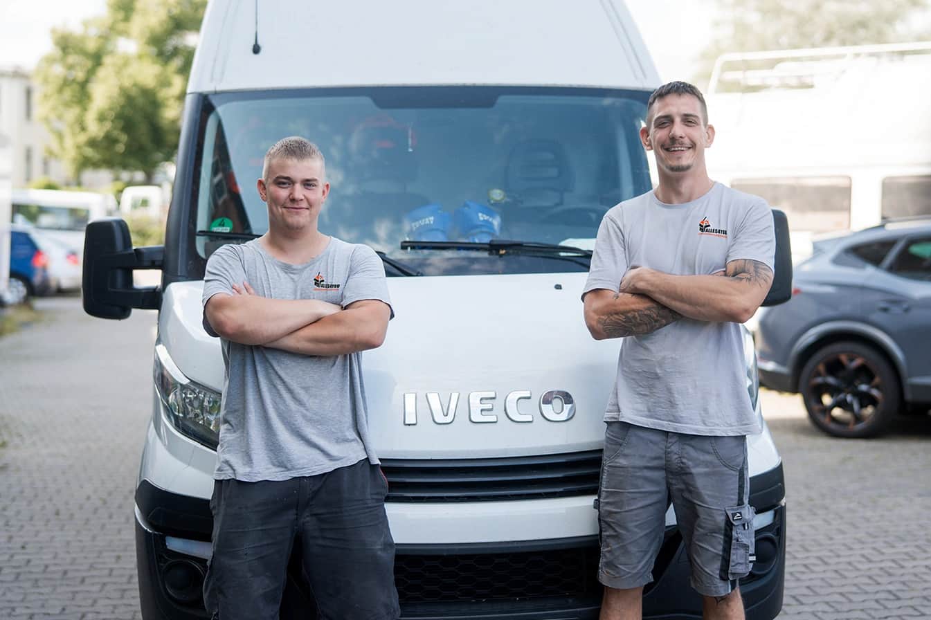 Two Alles4You crew members in company shirts in front of their white transport van in Berlin