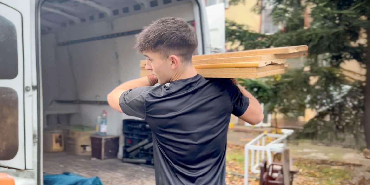Alles4You worker carrying dismantled furniture parts on his shoulder to an open van during a move in Berlin